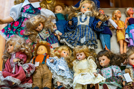 Close-up of a collection of antique porcelain dolls dressed in ornate vintage clothing, sitting in a wooden crate, detailed faces and hair, arranged in a group on display, visible price tags.