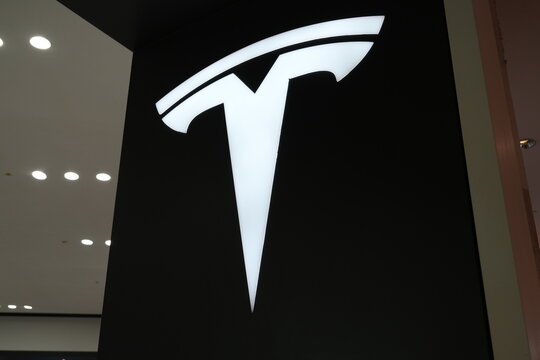 A glowing white Tesla logo on a black wall.