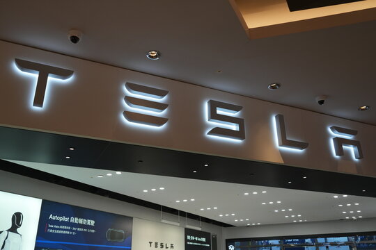 A large glowing Tesla sign inside a retail showroom.
