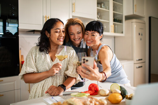 Friends taking a selfie with wine in a home kitchen