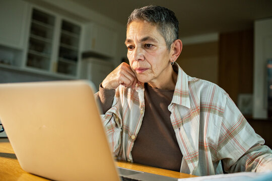 Focused senior woman working on laptop at home