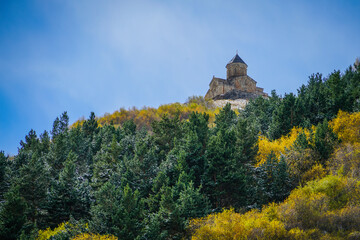Naklejka premium Gergeti Trinity Church, Stepantsminda, Georgia, overlooking a vibrant autumn forest beneath a clear blue sky.
