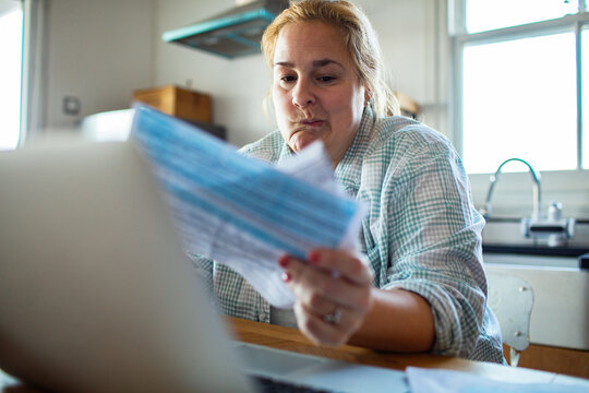 Concerned woman reviewing bills on laptop at kitchen table