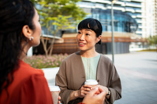 Two women chatting over coffee in modern city plaza