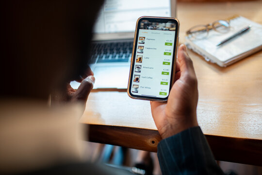 Customer ordering coffee on smartphone at cafe table