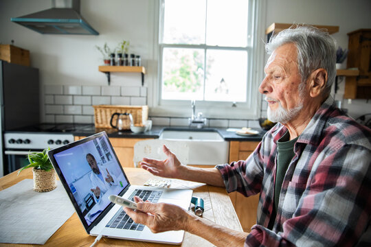 Older man on video call with doctor at home kitchen