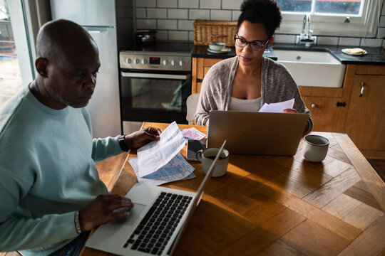 Couple managing household bills on laptops at kitchen table
