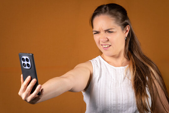 Mujer mirando su celular con dificultad, con una expresi&oacute;n de duda y problemas	