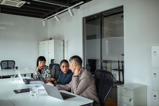 Three colleagues discussing project at laptop in modern office