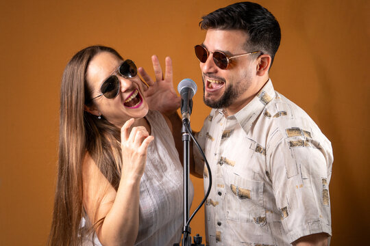 Pareja de hombre y mujer divirtiendose cantando karaoke juntos, con un micr&oacute;fono de pi&eacute;.