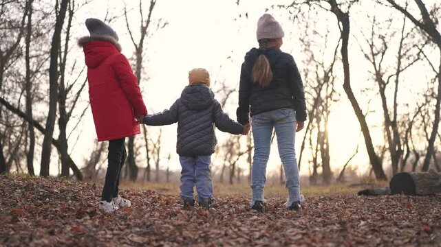 children walk in the forest in autumn park. happy family kid dream concept. group of children holding hands in nature jackets in the fall walking in a park in the forest. freedom childhood concept