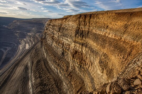 Edge of open-pit mine showing stratified layers of soil and rock, geological texture.