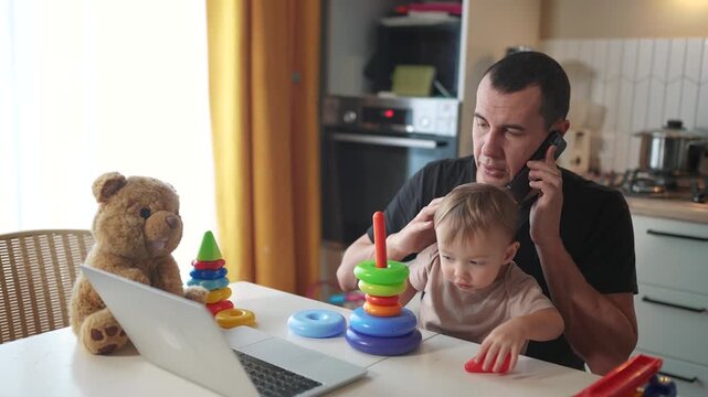 father working from home remotely with baby son in his arms. pandemic remote fun work business concept. father tries to work at home in kitchen, baby children interfere sitting on their hands