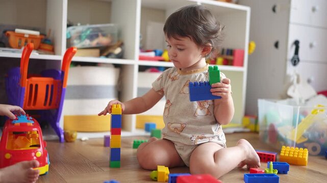 baby plays with blocks on floor in kindergarten. happy family kid concept. baby girl builds a tower from cubes and plays with toys. development of fine motor skills concept lifestyle