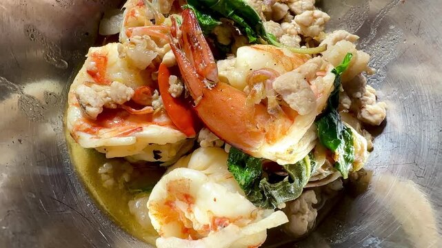 Stir-fried basil with large prawns and minced pork, served in a stainless steel bowl. A close-up, overhead shot of this popular Asian street food dish &ndash; a true Thai street food classic.