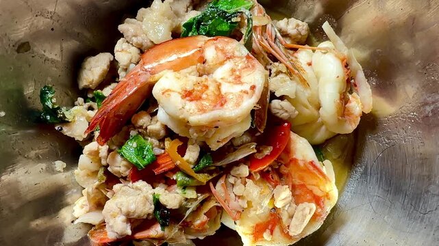 Stir-fried basil with large prawns and minced pork, served in a stainless steel bowl. A close-up, overhead shot of this popular Asian street food dish &ndash; a true Thai street food classic.