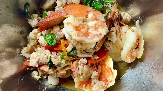 Stir-fried basil with large prawns and minced pork, served in a stainless steel bowl. A close-up, overhead shot of this popular Asian street food dish &ndash; a true Thai street food classic.