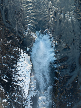 Aerial view of Dettifoss waterfall with powerful cascading water, rugged volcanic rock formations, and patches of snow in Nordurthing, Iceland.
