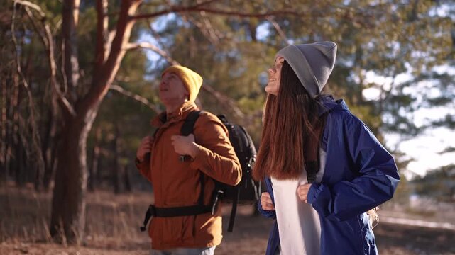 two hiker work as team. with backpacks walking in winter in a forest park in the sunny glare at sunset. Two tourists travel hiking in forest park sun, overcoming difficulties, teamwork concept
