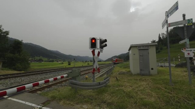 Railway crossing in Bavaria, Germany, with flashing lights and a closing gate as a red regional train speeds by. Cyclists pass nearby on a bike path, emphasizing the importance of caution and safety. 