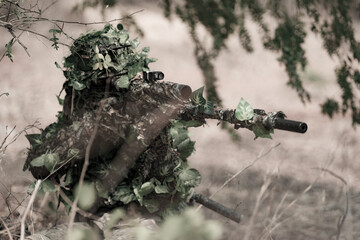 Fototapeta premium Soldier hides in forest using camouflage to blend with surroundings while waiting for target in daytime