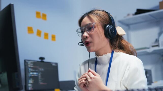 Confident Asian Female Customer Service Agent talking, typing and helping client via headset using computer in call center office. Call Center Representative Assisting a Customer During a Live Support