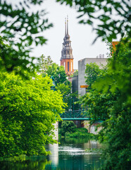 Malowniczy widok na wieże Katedry w Opolu wyłaniające się spośród soczystej zieleni drzew nad rzeką. Gotycka architektura w letniej ramie liści. © Henryk Niestrój