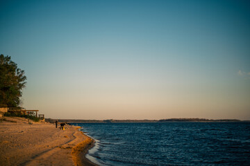 Obraz premium Golden hour on a sandy beach with calm blue water and distant treeline