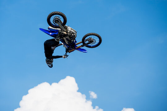 Motocross rider performing spectacular freestyle jump high in the air against blue sky, showcasing extreme sport, skill and adrenaline-filled action