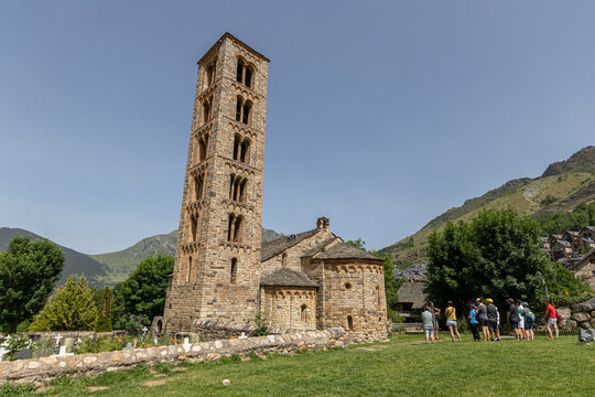 Taull, Spain. Exterior view of the twelfth century Sant Climent de Taull romanesque church featuring its iconic tall lombard bell tower, stone apses, and a tourist group on the grass