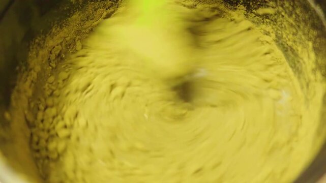 Close up shot of a green spatula mixing fine organic henna powder with water