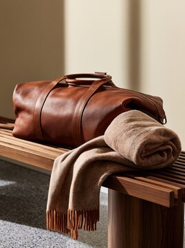 Luxury leather duffel bag with soft wool blanket on wooden bench in minimalist Scandinavian interior