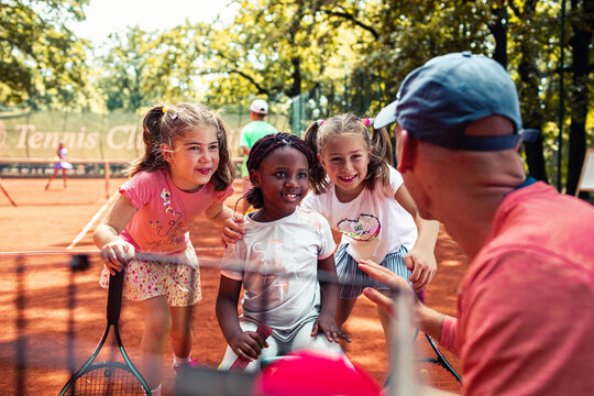 Young girls with tennis coach on outdoor clay court