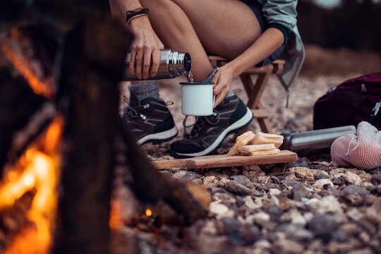 Camper pouring hot drink by campfire on rocky campsite