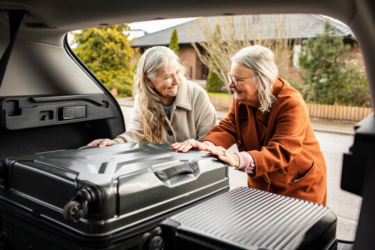 Senior women packing suitcases into car trunk on suburban street