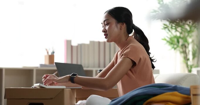 Asian woman calculating orders and preparing packages for online selling
