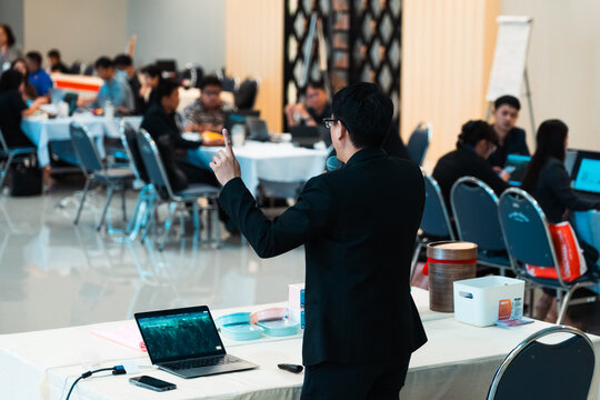 Confident male executive speaking into microphone and gesturing during engaging corporate seminar training session in modern conference hall with focused audience