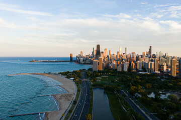 Fototapeta premium serene aerial drone shot of the chicago skyline with beachfront and cityscape in the background, featuring concrete, glass, and metal structures under a blue sky.