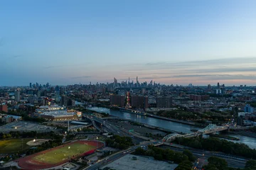 Aerial dusk panorama over Manhattan skyline with river, bridges, highways, stadium, and distant skyscrapers beneath calm blue evening sky and glowing lights, with aerial, manhattan, newyork, skyline © 21AERIALS