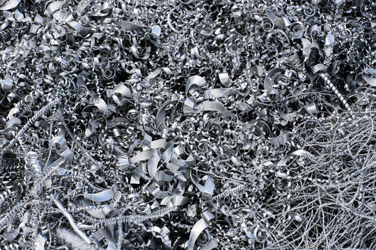 Metal shavings cover industrial surface. Curled steel chips form dense machining waste. Metalworking background shows production scrap. CNC cutting creates swarf. Recycling material fills frame.