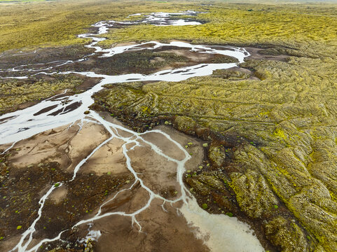 Aerial view of a complex braided river system winding through vibrant green moss-covered lava fields in Iceland.