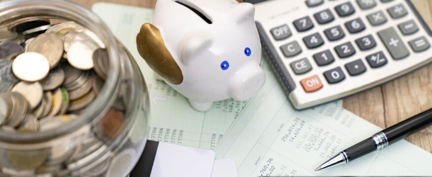 Glass jar holds coins, symbolizing savings. Piggy bank sits nearby, with blue eyes. Calculator rests beside papers, showing finances. Pen lies beside documents, ready for notes