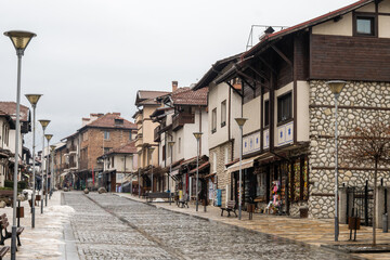 Fototapeta premium A quiet, wet cobblestone street lined with traditional stone and wood buildings in the historic old town, on a cloudy winter day in Bansko, Bulgaria.