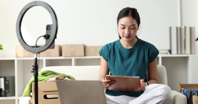Asian woman streaming product review for online clothing business using a ring light