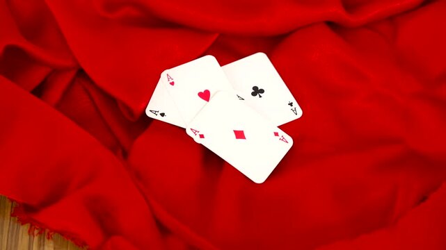 Playing cards ace of hearts spades diamonds clubs held by hand over red fabric background
