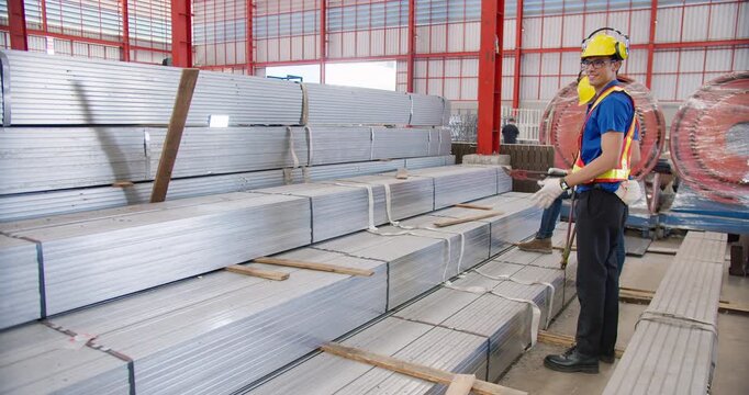 Two factory workers supervising inventory of galvanized steel at a manufacturing facility, ensuring quality control for the building materials supply chain.