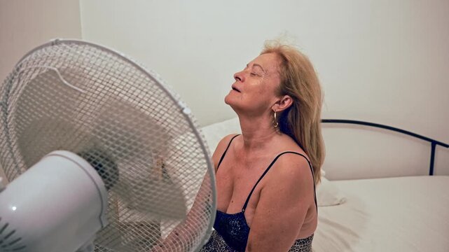 Senior woman cooling with electric fan