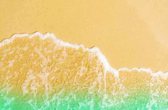 Top view of gentle ocean waves washing onto golden sandy beach with turquoise tropical water, creating a clean natural background for summer travel, coastal tourism, relaxation, and vacation concepts.