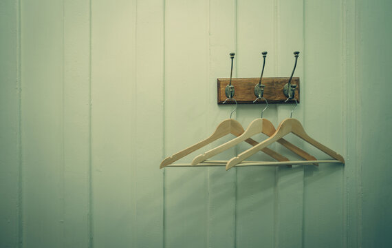 Minimal wooden clothes hangers hanging on vintage wall hooks against paneled interior wall. Organized home storage concept. Lifestyle, hospitality, and interior design themes. Hotel accommodation.