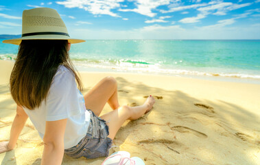 Back view of a female traveler relaxing alone on a quiet tropical beach with crystal clear sea and soft golden sand. Summer holiday, wellness retreat, tourism promotion, and mindful escape themes. © Fahroni